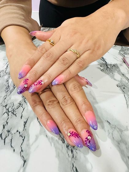 This stunning almond-shaped set features a pink-to-purple ombré with sparkling glitter tips. The hand-painted floral art on the accent nails adds a delicate, artistic touch.