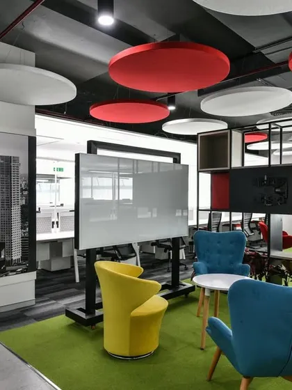 A collaboration zone with colorful armchairs and a mobile whiteboard. The ceiling features red and white acoustic panels to help control sound.