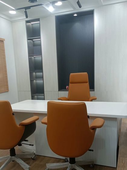 The main director's cabin, featuring a clean white desk, premium leather chairs, and a dark, textured back panel. The track lighting and built-in shelving add to the sophisticated and commanding feel of the space.