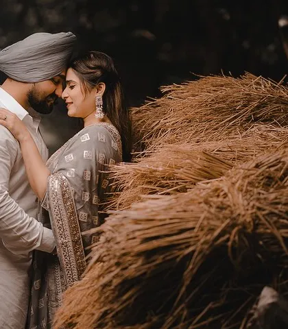 An intimate portrait of Aman and Simran next to a stack of hay. The rustic setting and their close embrace create a warm, earthy, and romantic image that feels straight out of a Punjabi love story.