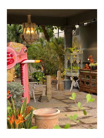 A vibrant pink elephant sculpture and an ornate birdcage are part of the whimsical landscape at Peacock Life. The design is a curated collection of art, furniture, and plants.
