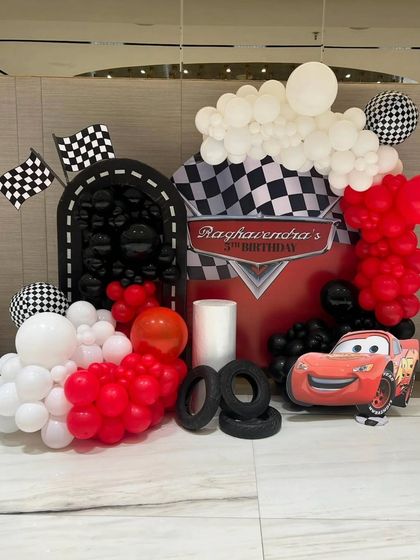 A fun photo corner for a Cars-themed birthday. The setup includes a custom backdrop, tire props, checkered flags, and a Lightning McQueen cutout.