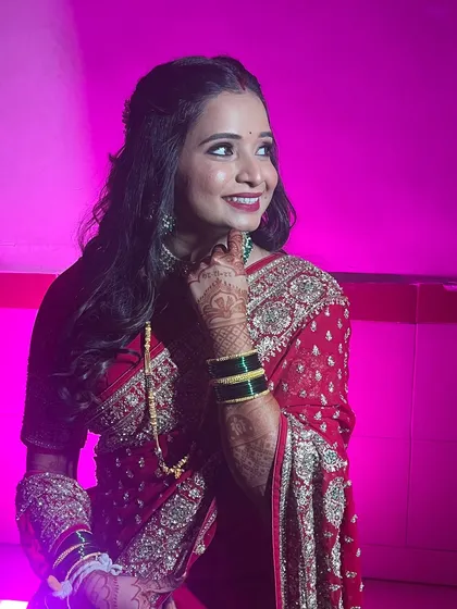 Rutuja's stunning reception look. The bold lip and smoky eye are perfect for an evening event, set against a dramatic pink light.