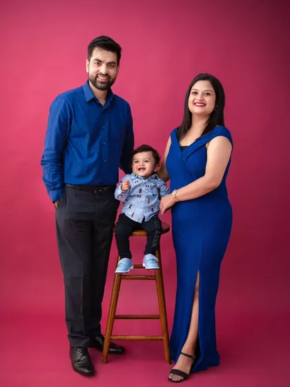 A vibrant and joyful family portrait. The family's royal blue outfits stand out beautifully against the solid magenta background, creating a bold and memorable image.