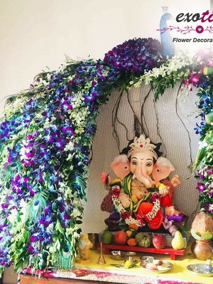 This Ganpati decoration is designed to resemble a magnificent peacock's tail, using an arch of blue and white orchids. The vibrant colors and flowing shape create a dynamic and beautiful setting for the idol.