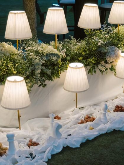 A detail shot of the organic dinner setup, with elegant table lamps nestled among wild florals and layered white drapes.