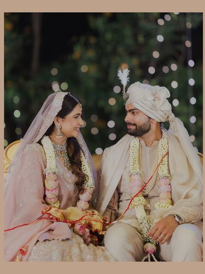 Seated together amidst the warm glow of celebration lights, the couple shares a look of love. This candid shot captures the quiet moments of connection during the wedding festivities.
