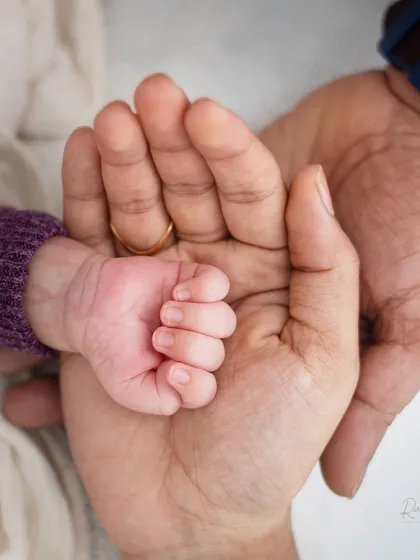 A newborn's tiny hand held securely in their parent's. This shot emphasizes the contrast in size and the protective love of a parent.
