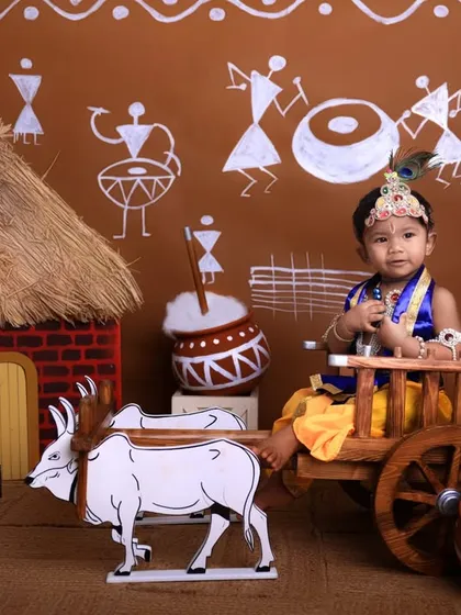 This little boy, dressed in a blue Krishna costume, sits thoughtfully in the bullock cart, creating a serene and captivating portrait against the traditional backdrop.