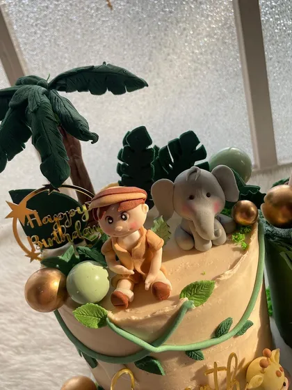 A close-up of the handmade toppers for a jungle-themed first birthday cake. I sculpted this little explorer and his elephant friend from fondant to create a personalized touch.