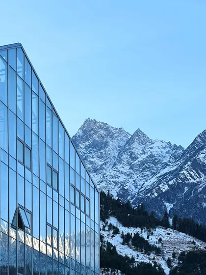 The Hamsa Resort in Manali features a modern glass and steel facade that reflects the surrounding Himalayan peaks. This design choice creates a direct visual dialogue between the structure and its environment, while the building itself incorporates traditional Kathkuni construction principles.