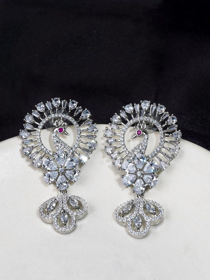 Diamond and silver peacock-style earrings on a clean white plate. The simple background ensures that the intricate design of the jewellery is the main focus.