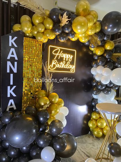 A close-up of the personalized 'KANIKA' sign and the black and gold balloon decor.