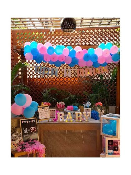 A full view of a gender reveal party setup. The decor includes a 'Boy or Girl' banner, a 'He or She' welcome sign, and light up 'BABY' marquee letters to create a fun and festive corner.