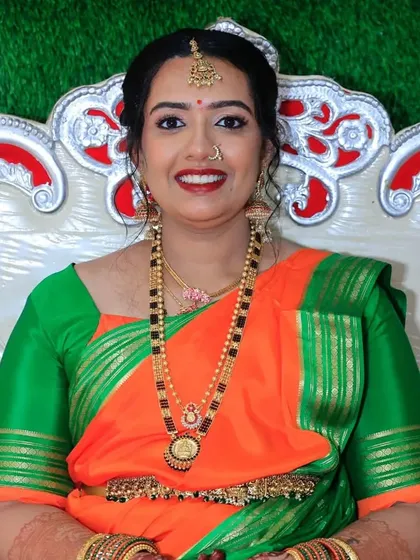 A beautiful portrait of Chandana, seated and glowing. Her makeup features a classic bold red lip and defined eyes, perfect for the celebratory occasion.