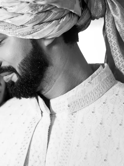 An artistic, tightly cropped black and white portrait that focuses on the groom's expression and the bride's subtle presence.