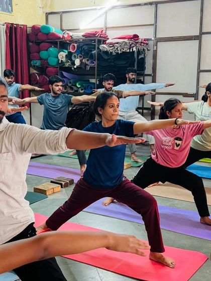 A class of students holds Virabhadrasana II (Warrior II). This powerful standing pose builds strength in the legs and focus in the mind. The collective determination is palpable.