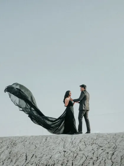A dramatic wide shot, showing the bride's black gown flowing in the wind against the vast, open sky. This kind of epic shot is a must-have for a destination pre-wedding shoot.
