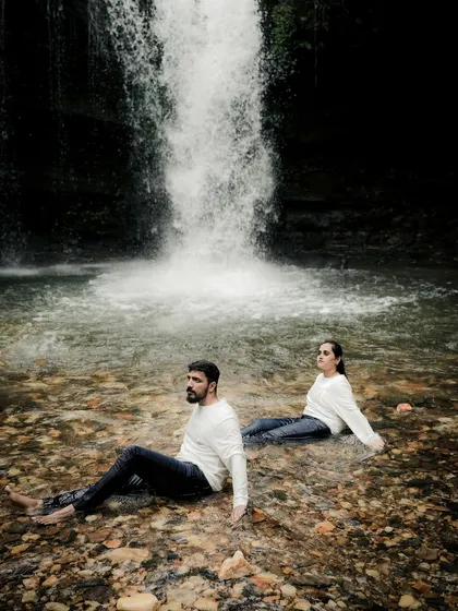 A wide shot of the couple sitting peacefully in the water at the base of a waterfall. This image has a serene and almost meditative quality, capturing a moment of shared tranquility.