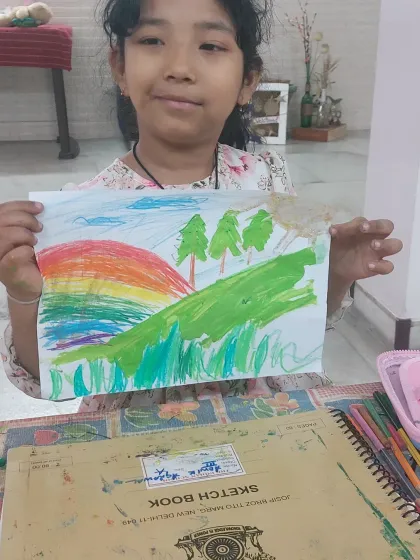 A young artist proudly displays her beautiful landscape painting. The blend of colors in the sky and the details in the scenery show her growing skills.