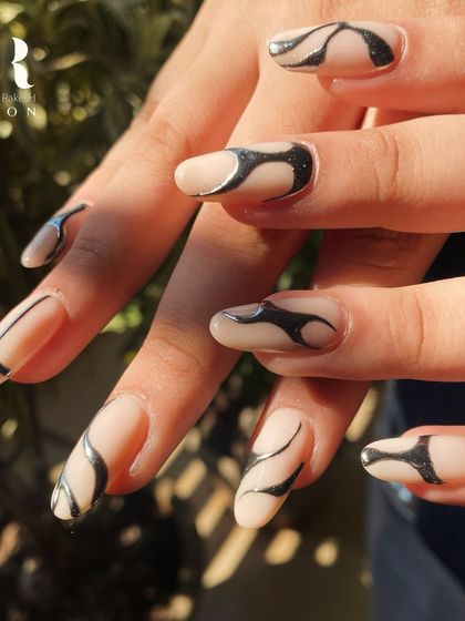A mesmerizing design with a touch of edge. We used a shimmering black polish to create these abstract, wavy patterns over a sheer nude base on long, almond-shaped nails.