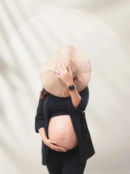 A chic and mysterious portrait. The mother-to-be uses a straw hat to playfully hide her face, creating a modern and stylish shot that focuses on her beautiful baby bump.