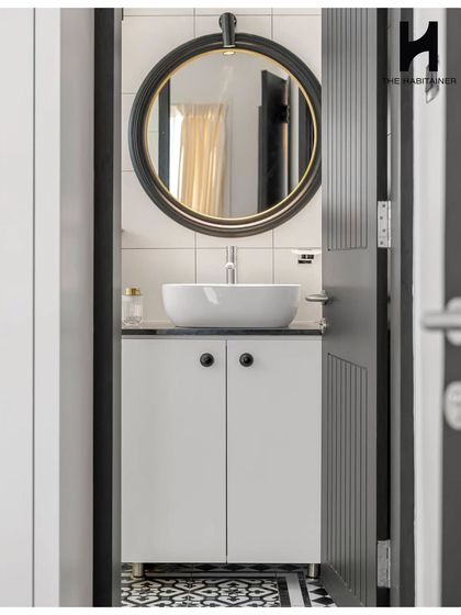 The chic washroom in the same home features bold black-and-white patterned floor tiles. A modern vessel sink sits atop a simple vanity, with a large round mirror and elegant lighting completing the look.