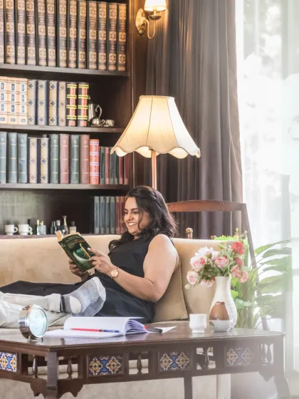 A candid shot of the bride relaxing on a sofa with a book, smiling. This lifestyle image adds a personal and serene touch to the pre-wedding gallery.