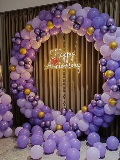 A first-anniversary celebration with a full circular balloon arch in shades of purple and gold, and a '1' foil balloon.