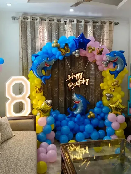 A fun Baby Shark theme for an 8th birthday party at home. This setup features a circular balloon arch with shark foils and a large marquee number '8'.