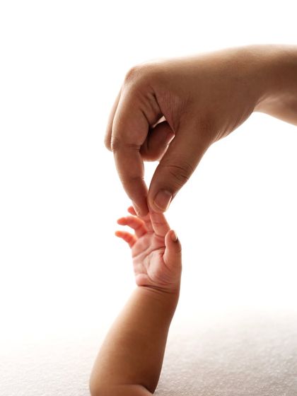 An adult's finger gently holding a newborn's tiny hand. A simple, powerful image showing the contrast in size.