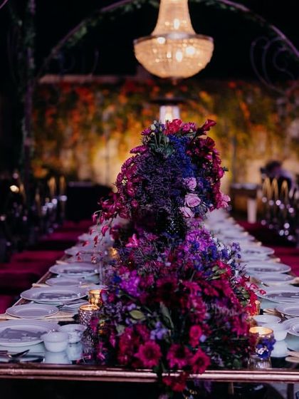 The long table setup for the reception dinner, featuring a lush, dramatic floral runner in deep jewel tones and elegant chandeliers.