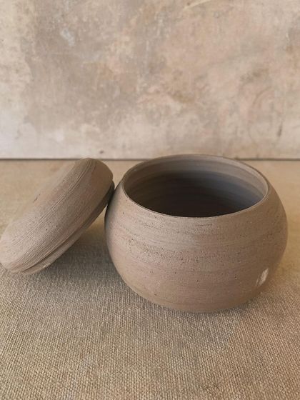 Another lovely unglazed lidded jar. The subtle lines from the throwing process and the earthy texture give this piece a quiet, minimalist beauty. We encourage students to appreciate the form even before glazing.