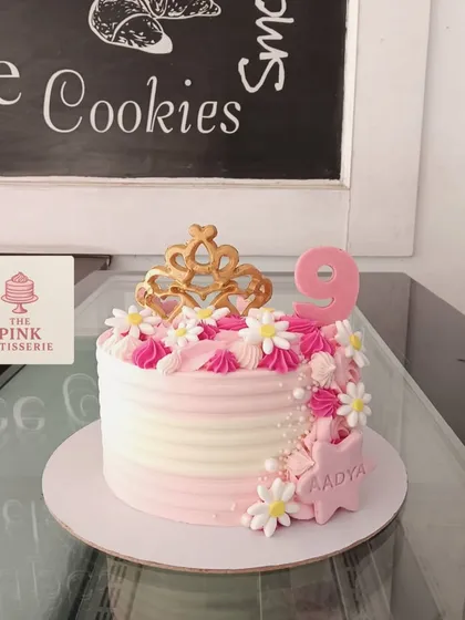 A pretty pink and white cake for Aadya's 9th birthday, decorated with a crown, daisies, and a personalized star.