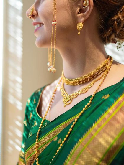 A close-up on the details of the Marathi bridal look. Here you can see the layered gold necklaces, the classic nath, and the intricate design of the green Paithani saree.