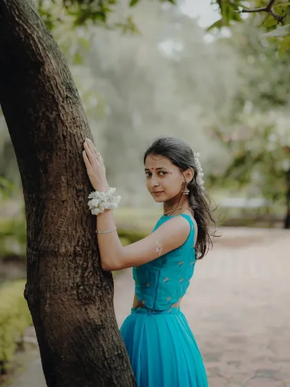 Leaning against a tree, this portrait captures a serene and slightly shy expression, reflecting the gentle nature of Radha.
