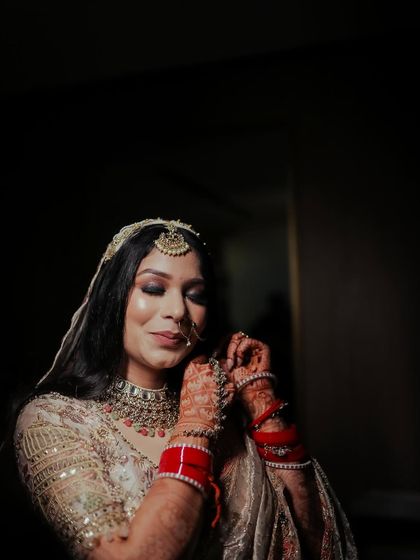 A bride getting ready, adjusting her jewelry in a dimly lit room.