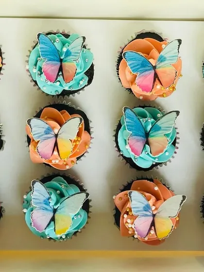 A top-down view of the peach and blue butterfly cupcakes, showing the arrangement in a box of twelve. The sprinkle of sugar pearls adds a final touch of sophistication.