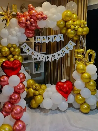 A festive 50th anniversary celebration setup indoors. I created a full balloon arch using a classic combination of red, gold, and white balloons, complemented by a 'Happy Anniversary' banner and large '50' foil numbers.