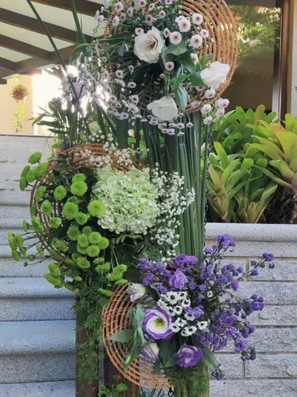 We see floral design as a form of art. This sculptural, multi-tiered floral installation combines vibrant greens, purples, and whites with natural woven textures to create a unique and modern statement piece for a corporate space.