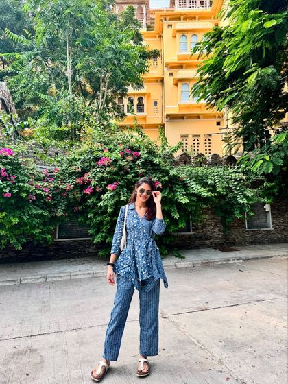 Posing in my blue printed co-ord set in Udaipur. The vibrant yellow building and lush greenery create a beautiful contrast, showing how your outfits can interact with your travel surroundings.
