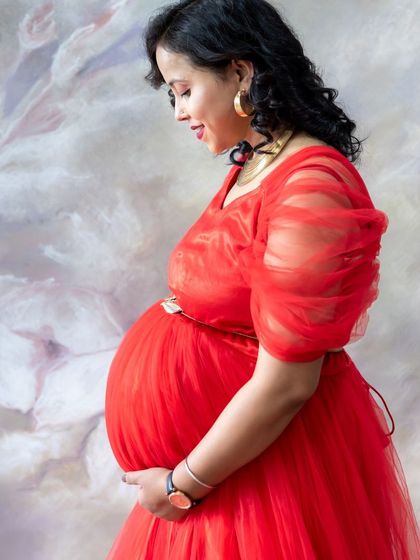 A classic side-profile portrait in the studio. This shot beautifully captures the curve of the baby bump in a vibrant red gown.