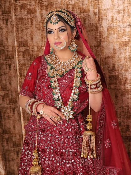 A full-length view of a bride in a classic red embroidered lehenga, complete with a heavy jewellery set and kalire. This is the quintessential bridal look, available for rent.