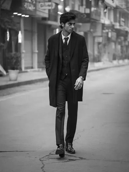 A full-length shot of a model in a three-piece suit walking down an empty street. This black and white image has a classic, cinematic feel, like a still from a film.
