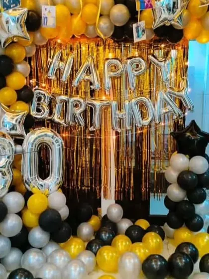 A grand 30th birthday celebration at home. This full backdrop uses a gold shimmer curtain, a balloon arch in black, gold, and silver, and large "30" foil balloons to mark the special milestone.