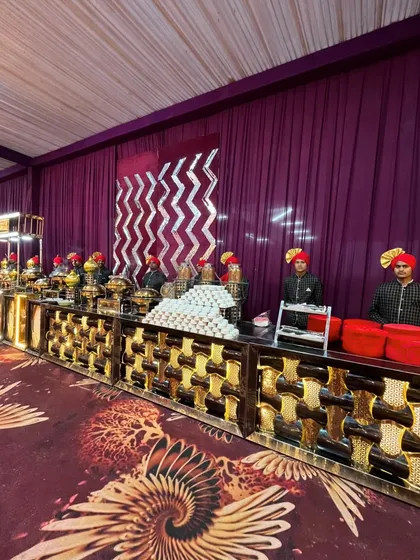 A wide shot of a buffet line designed with a striking gold and black patterned counter. The staff in matching uniforms and turbans add a touch of coordinated professionalism to the royal theme.