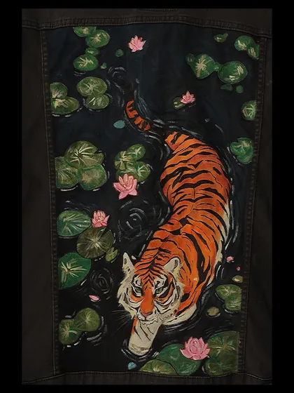 A tiger wading through a lily pond, painted on the back of a dark jacket. For this piece, I focused on the contrast between the tiger's bold stripes and the delicate pink flowers, creating a serene yet powerful nature scene.
