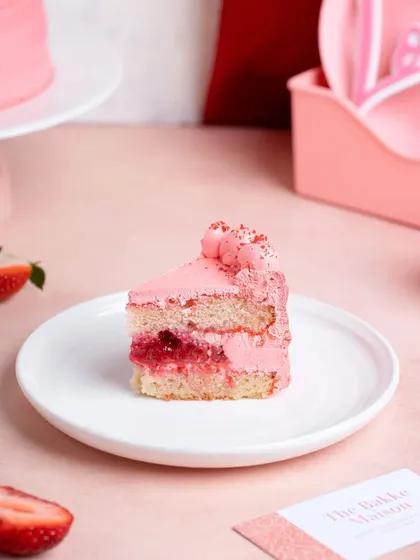 A slice of delicate strawberry cake on a white plate, styled for Valentine's Day. The pink and red color scheme creates a romantic mood.