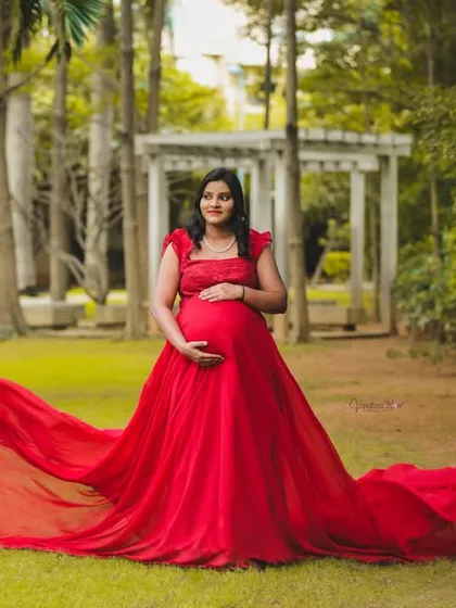 A stunning solo portrait of a mother-to-be in a vibrant red flowing gown, standing in a lush green park. This shot is all about celebrating the power and beauty of pregnancy.