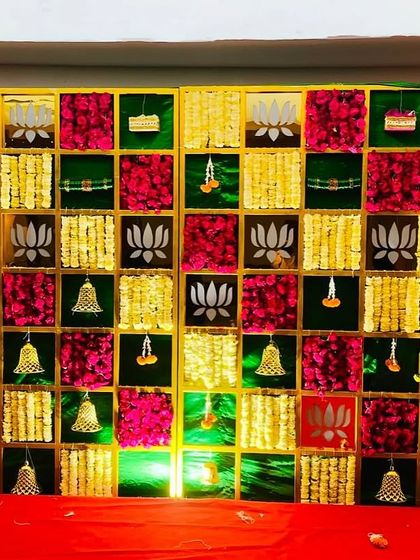 A colorful checkerboard backdrop for a Seemantham ceremony. This design uses panels of magenta, yellow, and green fabric, accented with hanging bells and lotus motifs for a festive look.